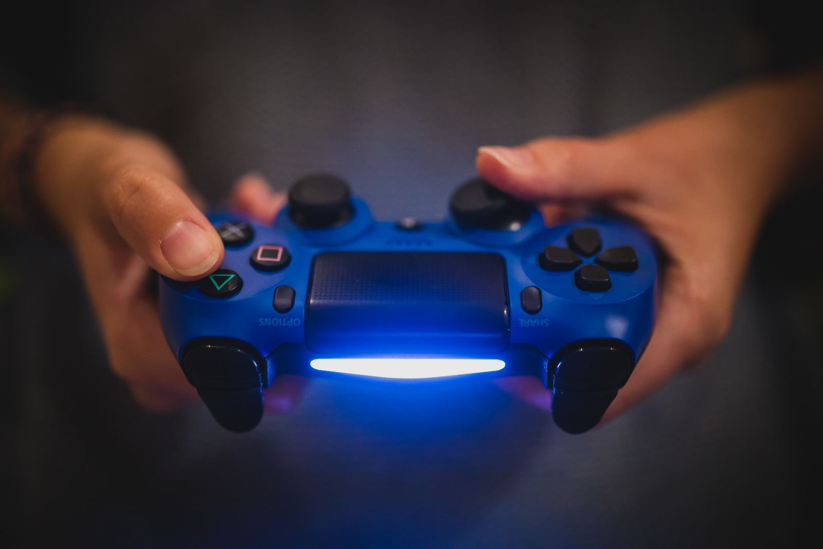 Close up of someone holding a blue, lit-up Playstation controller